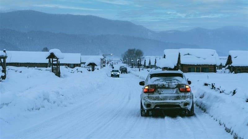 Cars driving down a snow-covered village road in heavy winter conditions