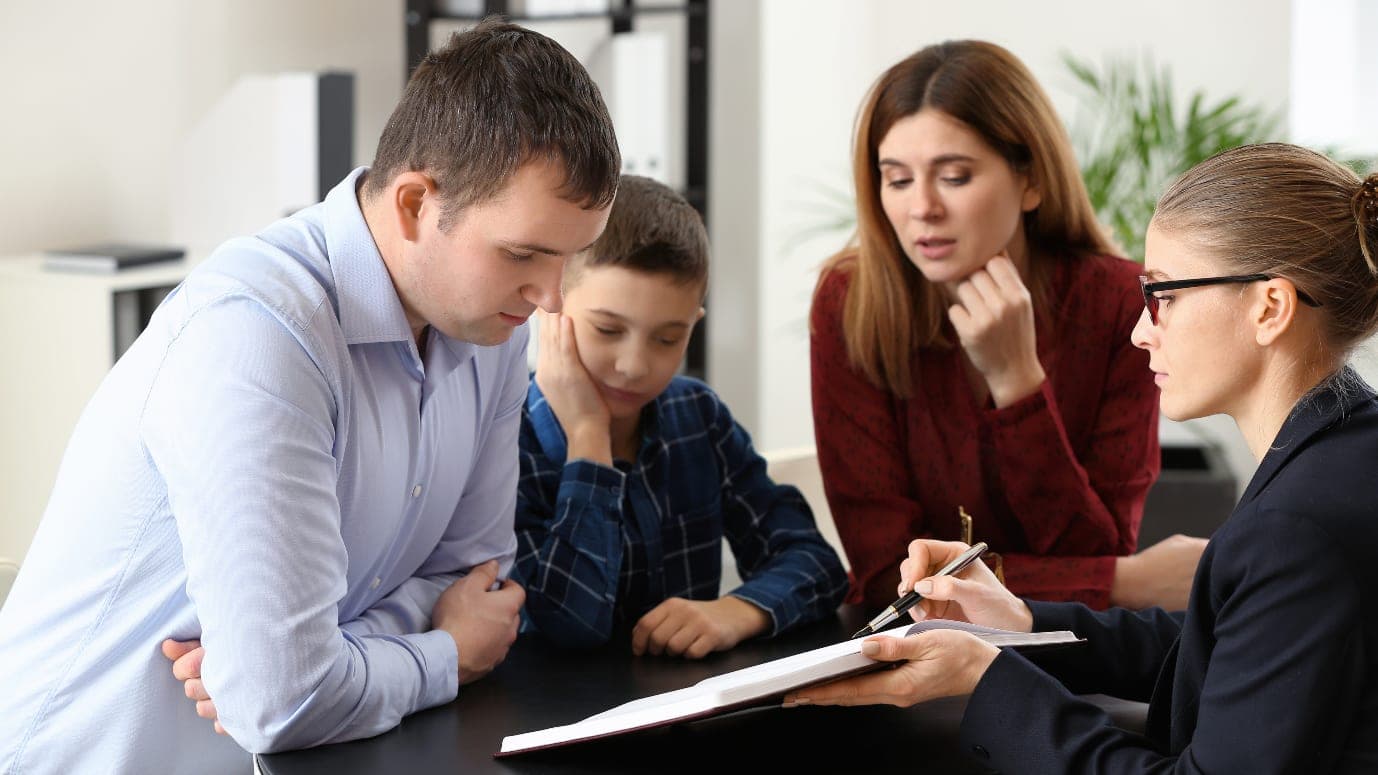 A lawyer taking notes across a table from two parents and a child