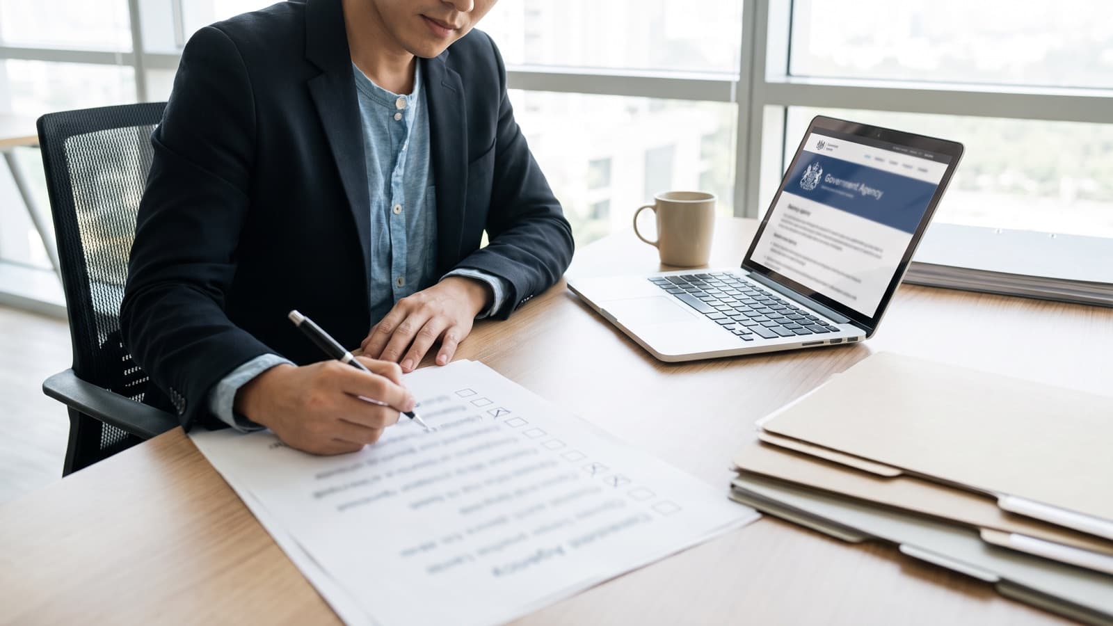 Entrepreneur checking items off a printed checklist beside a laptop showing a government registration page