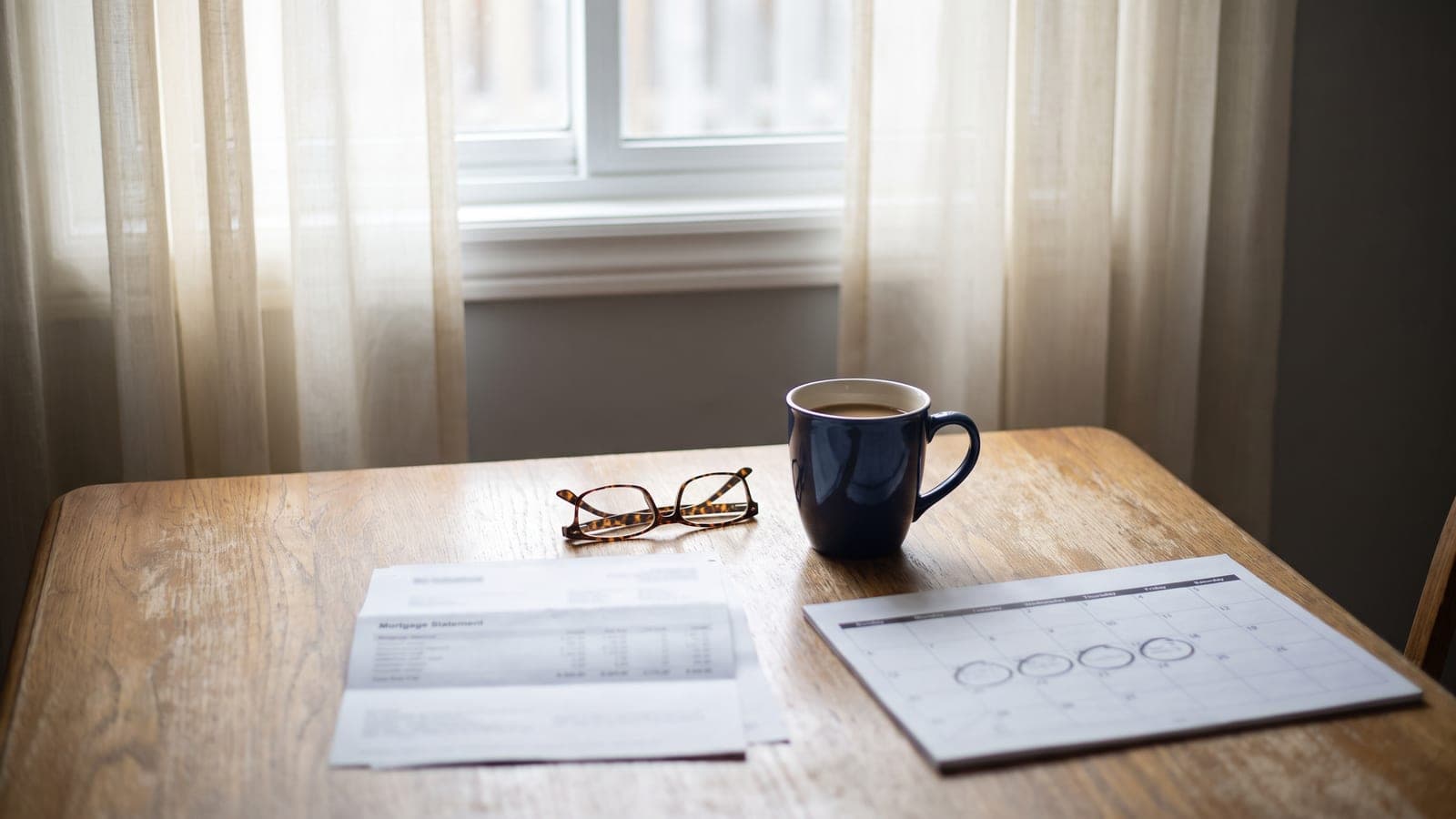 A mortgage statement and a wall calendar on a kitchen table in a quiet Ontario home, morning light through the window