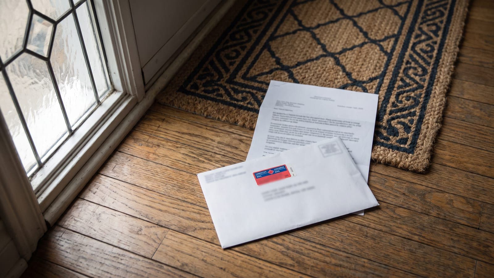 A registered mail envelope and a folded legal notice lying on a hallway floor just inside a front door