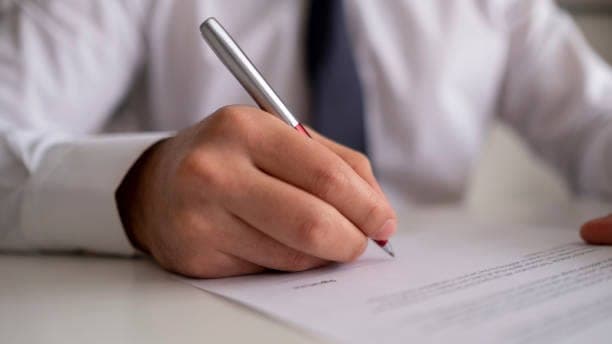A person signing a document at a desk with a silver pen